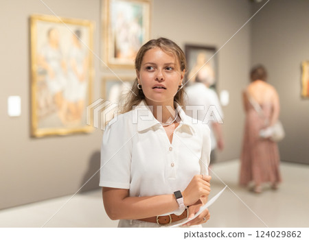 Woman with sheet piece of paper in hands view pictures and icons in museum hall Woman with sheet piece of paper in hands view pictures and icons in museum hall 124029862