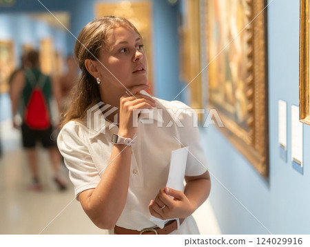 Woman with sheet piece of paper in hands view pictures and icons in museum hall Woman with sheet piece of paper in hands view pictures and icons in museum hall 124029916