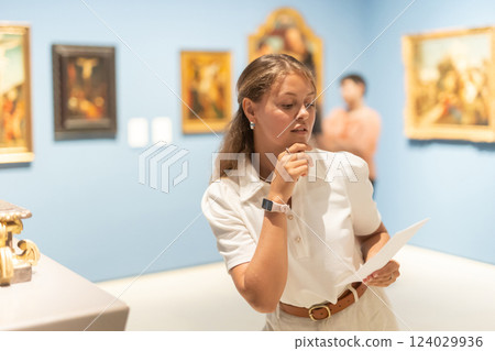 Woman with sheet piece of paper in hands view pictures and icons in museum hall 124029936