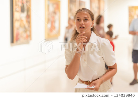 Woman with sheet piece of paper in hands view pictures and icons in museum hall Woman with sheet piece of paper in hands view pictures and icons in museum hall 124029940