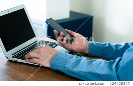 A man operating a smartphone and a computer 124030265