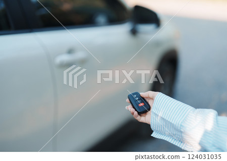 Hand holding car remote control, smart key to lock or unlock doors of white car. Safety, travel and transportation concept Hand holding car remote control, smart key to lock or unlock doors of white car. Safety, travel and transportation concept 124031035