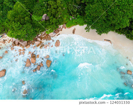 The waves crash against the rocky shore, with a white sandy beach and emerald green foliage creating a tranquil coastal scene. Anse Lazio, Seychelles. The waves crash against the rocky shore, with a white sandy beach and emerald green foliage creating a tranquil coastal scene. Anse Lazio, Seychelles. 124031330