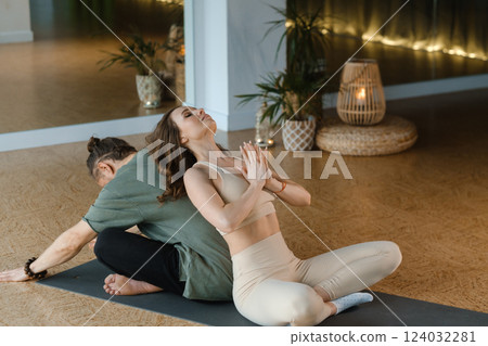 Couple practicing partner yoga in a serene indoor studio during an evening session with warm lighting and calming atmosphere Couple practicing partner yoga in a serene indoor studio during an evening session with warm lighting and calming atmosphere 124032281