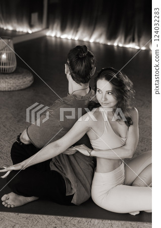 Couple practicing partner yoga in a serene indoor studio during an evening session with warm lighting and calming atmosphere Couple practicing partner yoga in a serene indoor studio during an evening session with warm lighting and calming atmosphere 124032283