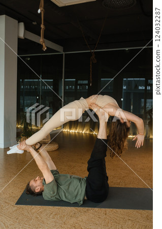 Couple practicing acro yoga in a spacious studio with soft lighting during an afternoon session Couple practicing acro yoga in a spacious studio with soft lighting during an afternoon session 124032287