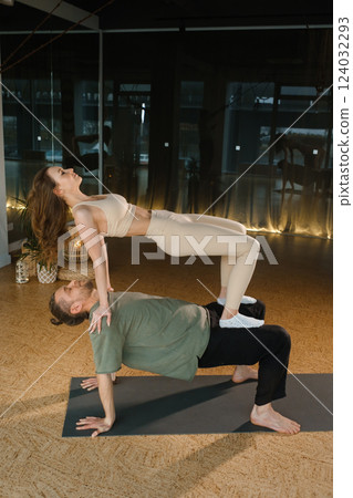 Yoga practice involving a woman executing a challenging pose on a man's back in a modern studio setting during a morning session 124032293