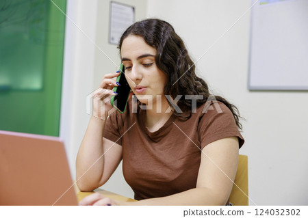 A woman talking on the phone while using a computer A woman talking on the phone while using a computer 124032302