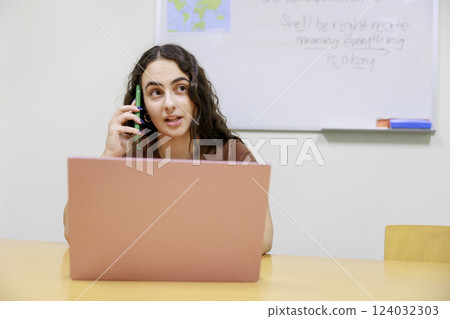 A woman talking on the phone while using a computer A woman talking on the phone while using a computer 124032303