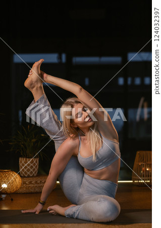 Yoga practitioner demonstrates impressive flexibility in serene studio setting during evening relaxation session with soft lighting 124032397