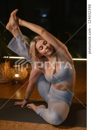 Yoga practitioner demonstrates impressive flexibility in serene studio setting during evening relaxation session with soft lighting 124032398
