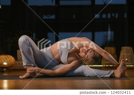 Yoga practitioner performs advanced stretch in serene indoor setting during twilight hours, highlighting flexibility and calmness 124032411