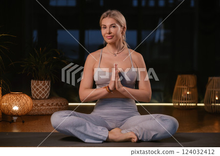 Woman practicing yoga in a modern studio with soft lighting while sitting in a meditative pose and hands in prayer position 124032412
