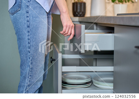 Person opening kitchen drawer with cutlery in cabinet 124032556