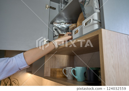 Woman reaching for jar in kitchen cabinet with stored cooking ingredients 124032559