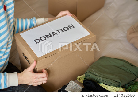 Woman holding donation box with clothes on bed 124032590