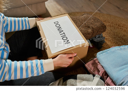Woman packing donation box, preparing used clothes for charity Woman packing donation box, preparing used clothes for charity 124032596