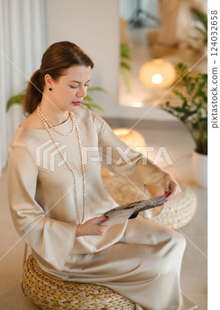 Girl in beige dress with beads with a fan of Tarot cards indoors . Tarot cards in the hands of a fortune teller Girl in beige dress with beads with a fan of Tarot cards indoors . Tarot cards in the hands of a fortune teller 124032658