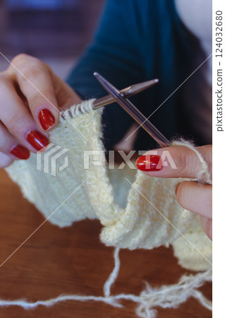 Women hands holding knitting needles and yellow cotton knitted work. Knitting woman with bobbins of yarn and yellow knitwear. Needlework in process. Knitting hobby. Knitter work. Women hands holding knitting needles and yellow cotton knitted work. Knitting woman with bobbins of yarn and yellow knitwear. Needlework in process. Knitting hobby. Knitter work. 124032680