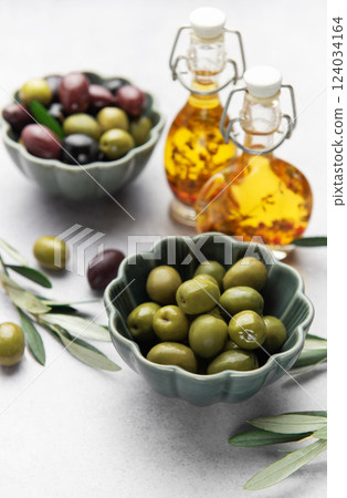 Bowls of green and black olives with olive oil bottles and olive branches on marble table 124034164