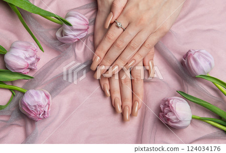 Woman showing nude manicure with engagement ring near pink tulips Woman showing nude manicure with engagement ring near pink tulips 124034176
