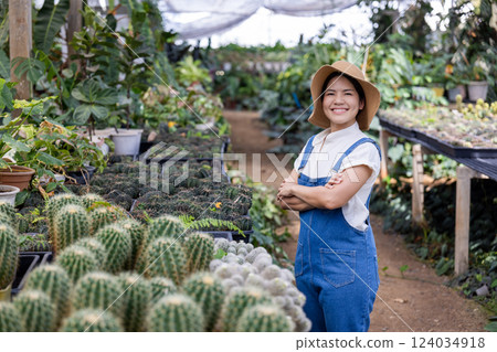 Happy female gardener in green house full of plants Happy female gardener in green house full of plants 124034918