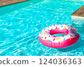 Pink donut-shaped inflatable float in turquoise swimming pool with wooden deck on a sunny day 124036363