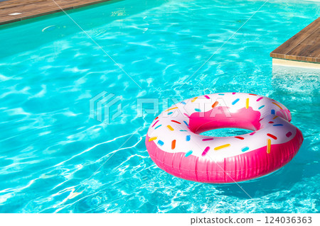 Pink donut-shaped inflatable float in turquoise swimming pool with wooden deck on a sunny day Pink donut-shaped inflatable float in turquoise swimming pool with wooden deck on a sunny day 124036363