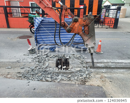 Construction work is underway street, featuring hydraulic excavator breaking concrete near drainage grate. scene conveys sense of urban Construction work is underway street, featuring hydraulic excavator breaking concrete near drainage grate. scene conveys sense of urban 124036945