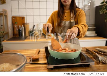 Happy asian woman in apron preparing meal in a stylish home kitchen Happy asian woman in apron preparing meal in a stylish home kitchen 124037421