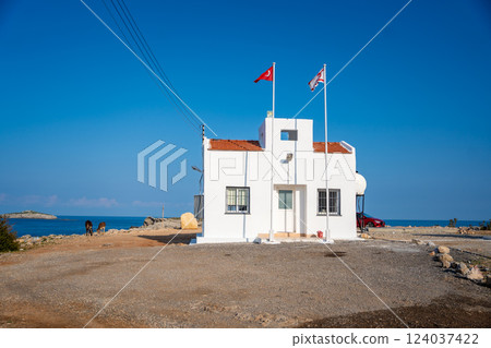 Small white building at the northeasternmost cape of Cyprus with the flags of Turkey and Northern Cyprus. Islands farthest point and serves as a symbol of political and territorial presence 124037422