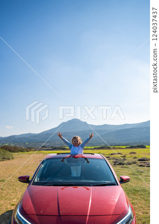 Little girl joyfully sticks out of car sunroof with raised hands against the backdrop of mountains in Northern Cyprus. The image symbolizes freedom, adventure, and the excitement of travel with child 124037437