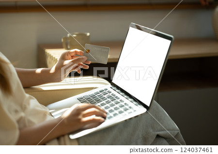 Close up of woman using a laptop while holding a credit card for online transactions 124037461