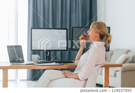 Eating an apple. Female stock broker in formal wear is working in the office Eating an apple. Female stock broker in formal wear is working in the office 124037993