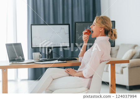 Eating an apple. Female stock broker in formal wear is working in the office Eating an apple. Female stock broker in formal wear is working in the office 124037994