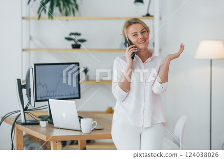 Using smartphone to communicate. Female stock broker in formal wear is working in the office 124038026