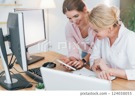Talking with each other. Two female stock brokers in formal wear is working in the office by pc Talking with each other. Two female stock brokers in formal wear is working in the office by pc 124038055