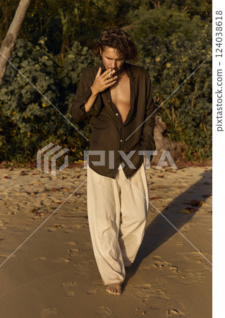 smoking boy on the beach at sunset. handsome wet man walking on sand smoking boy on the beach at sunset. handsome wet man walking on sand 124038618