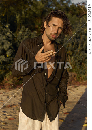 smoking boy on the beach at sunset. handsome wet man walking on sand smoking boy on the beach at sunset. handsome wet man walking on sand 124038619