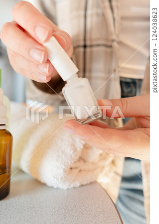 Nail care for weak nails: woman pushes back cuticles and applies serum for deep restoration of the nail plate. 124038623