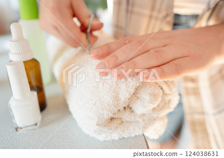 Nail treatment process: woman pushes back cuticles and applies vitamin-rich polish to restore nail structure. 124038631