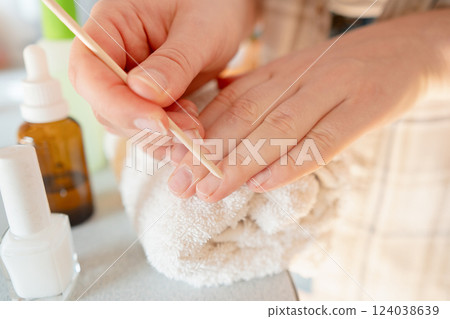 Woman cares for her nails by pushing back cuticles and applying strengthening polish for nail treatment. 124038639