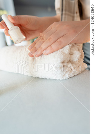 A woman gently pushes back the cuticle, preparing to apply treatment polish to strengthen brittle nails. 124038649