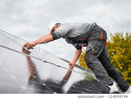 Man electrician mounting photovoltaic solar panels on roof of house. Engineer in helmet installing solar module system with help of hex key. Concept of alternative, renewable energy. 124039744