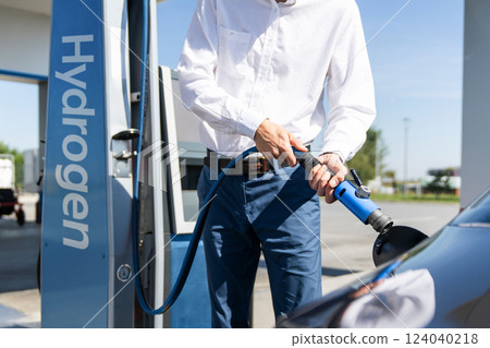 Man holds a hydrogen fueling nozzle on a hydrogen filling station. Refueling car with hydrogen fuel Man holds a hydrogen fueling nozzle on a hydrogen filling station. Refueling car with hydrogen fuel 124040218