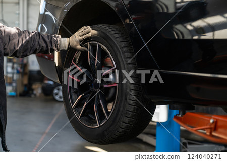 Serviceman checks car suspension on a column lift in car service. 124040271