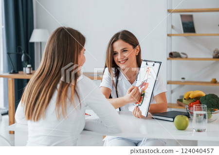 Woman showing illustration to the female customer. Professional medical worker in white coat is in the office 124040457