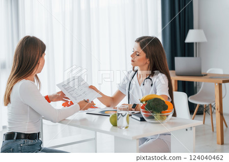 Female visitor is sitting with doctor. Professional medical worker in white coat is in the office 124040462