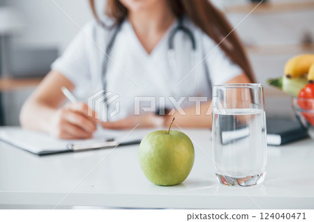 Woman writing information into the notepad. Professional medical worker in white coat is in the office 124040471