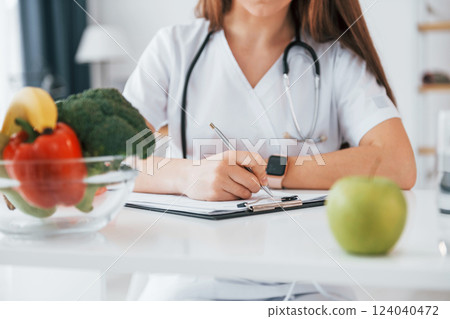 Woman writing information into the notepad. Professional medical worker in white coat is in the office 124040472
